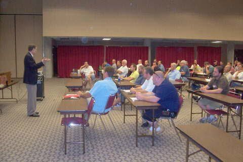 A man is giving a presentation to a group of people sitting at tables.