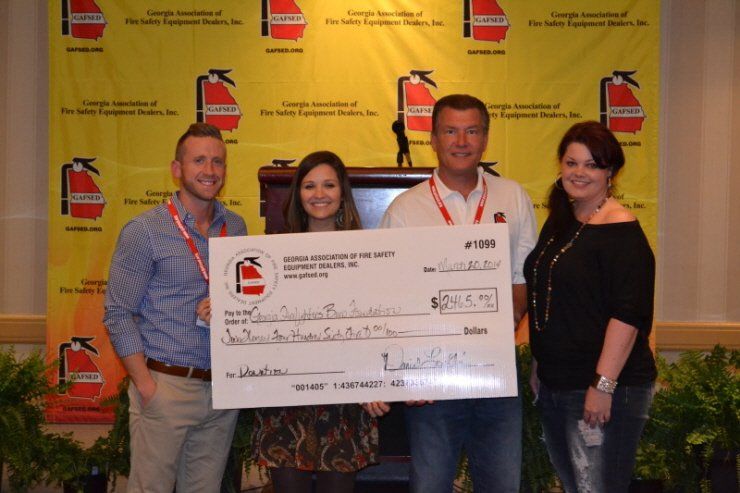 A group of people holding a large check in front of a fire extinguisher wall.