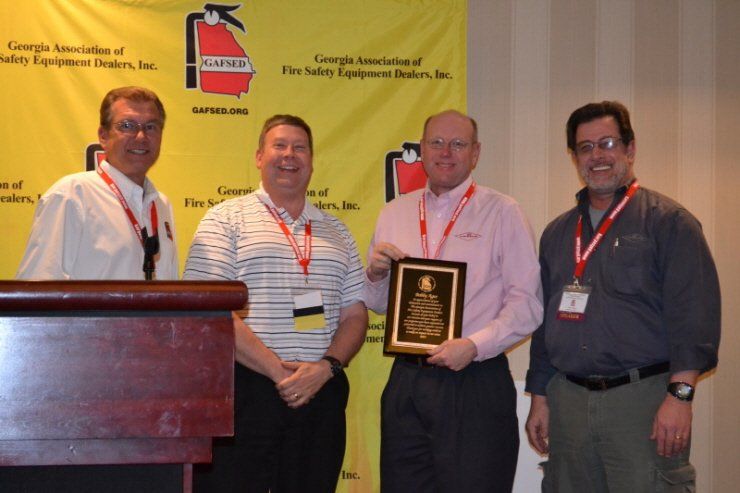 Four men standing in front of a podium holding a plaque