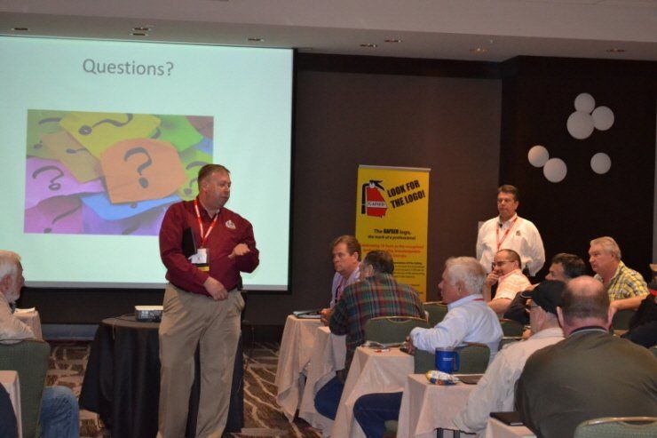 A man stands in front of a screen that says questions