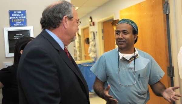 A man in a suit and tie is talking to a surgeon in a hospital room