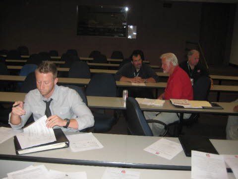 A man in a tie sits at a desk in a classroom
