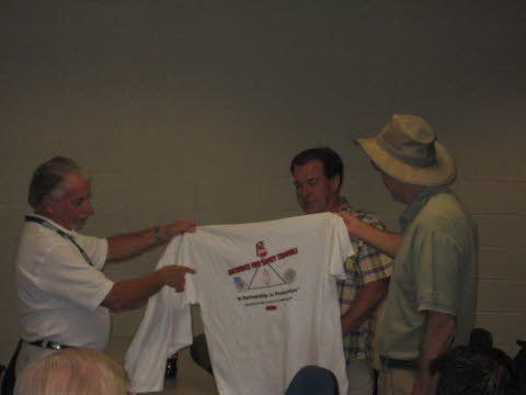 Three men are holding up a white t-shirt with a red arrow on it