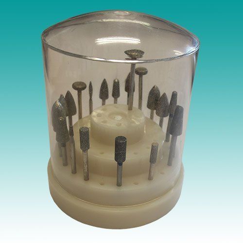 Doorzichtige cilindrische koffer met diverse kleine metalen roterende frezen op een beige voet.