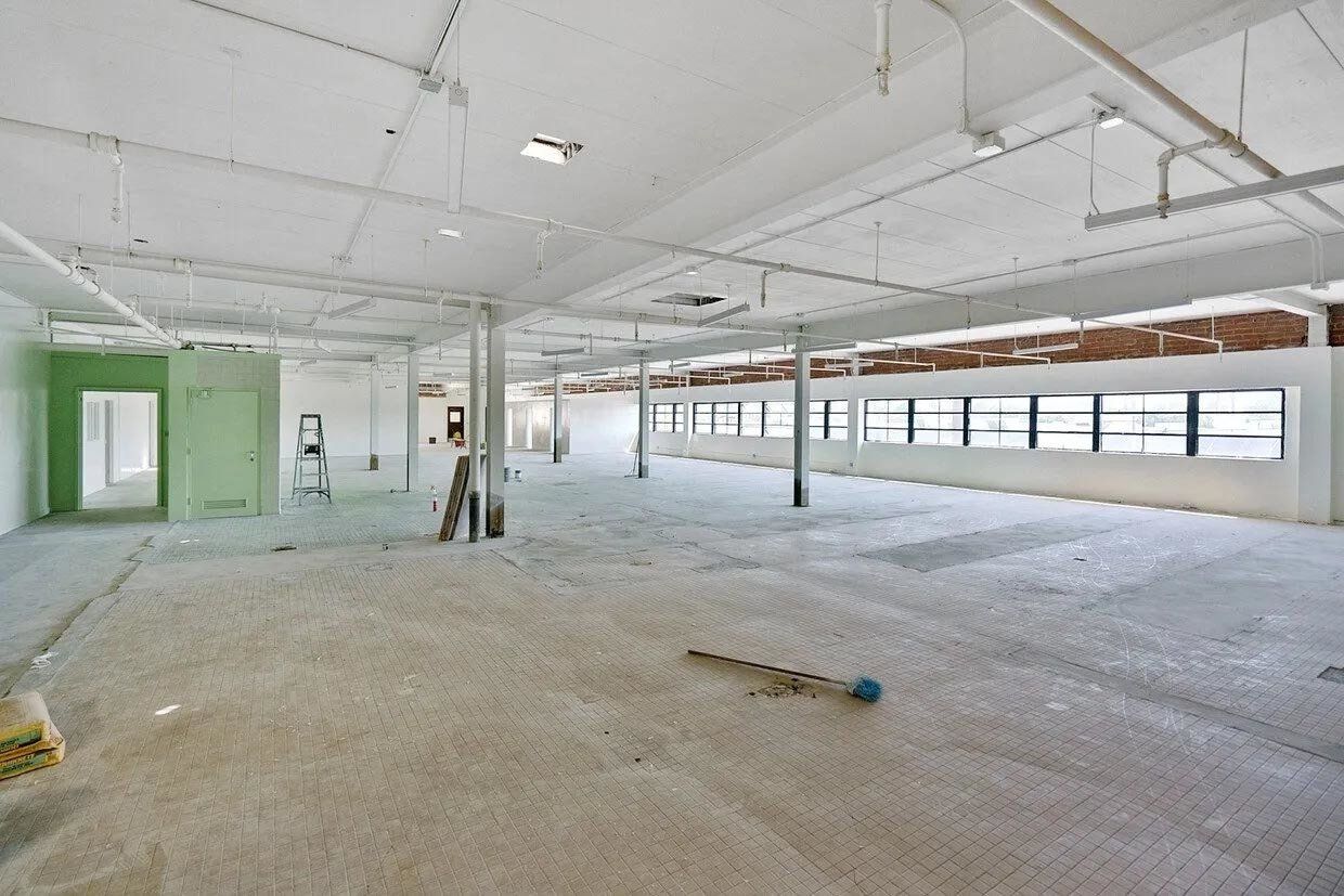 A large empty room with a lot of windows and a ladder on the floor.