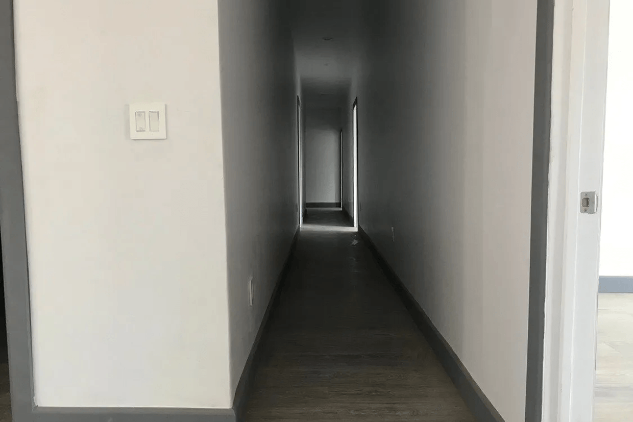 A long hallway in a house with white walls and a door.