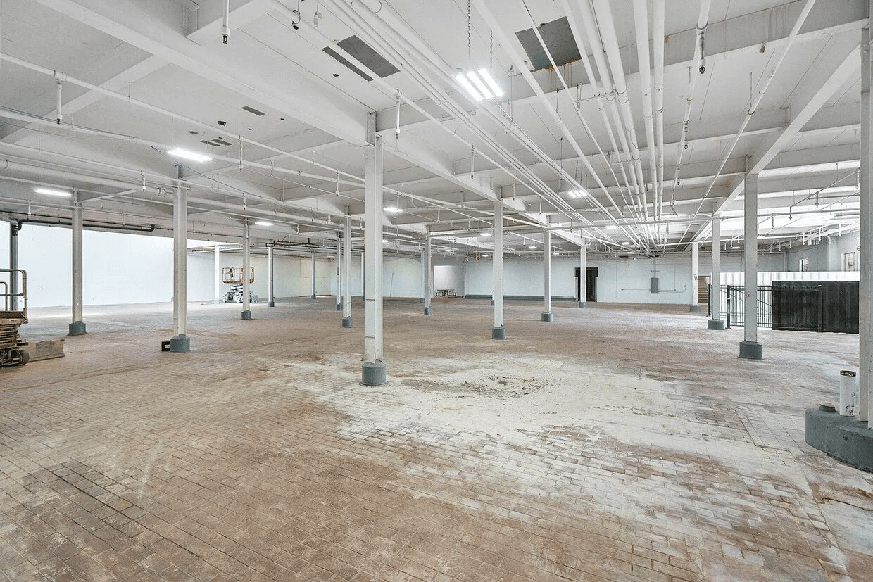 A large empty warehouse with a lot of pipes hanging from the ceiling.