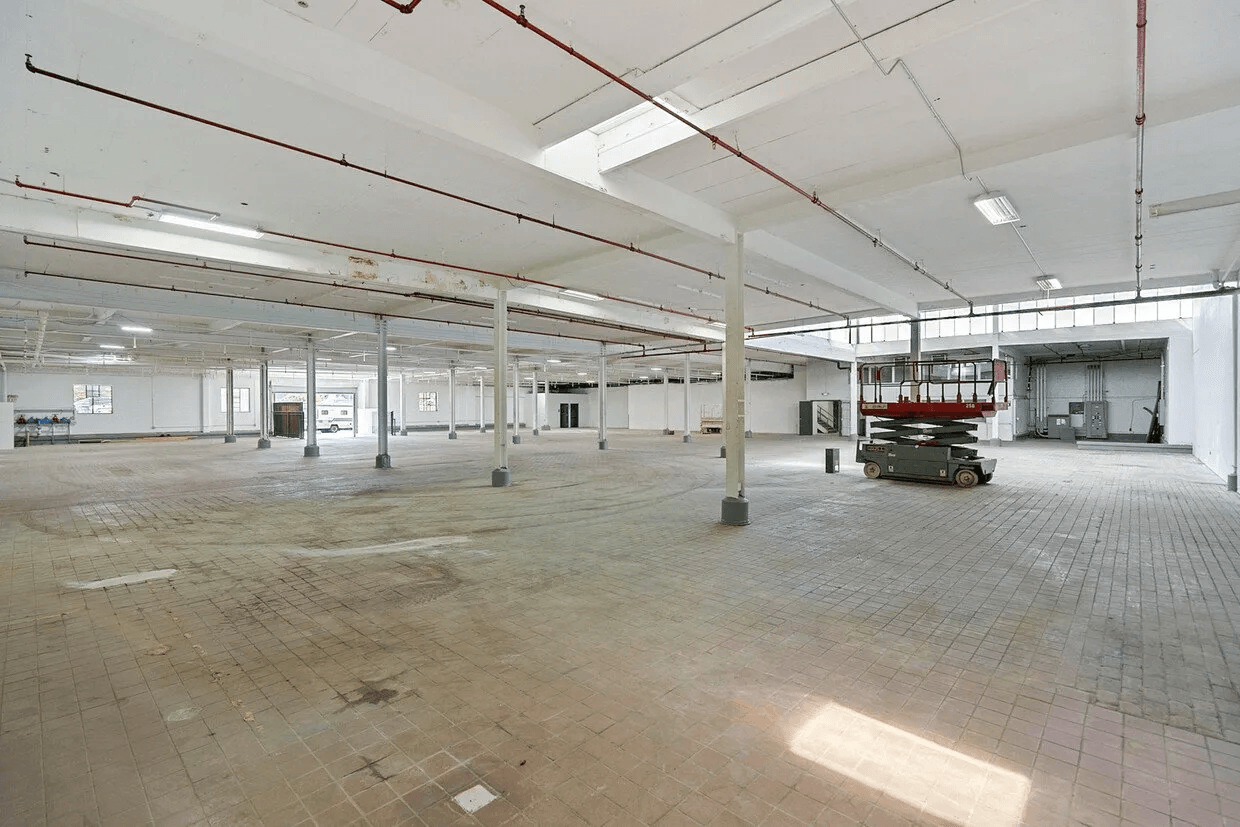 A large empty warehouse with a red scissor lift in the middle.