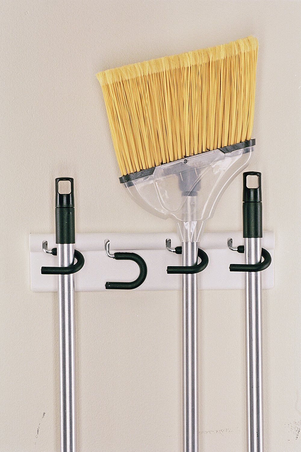 A broom and mop are hanging on hooks on a wall