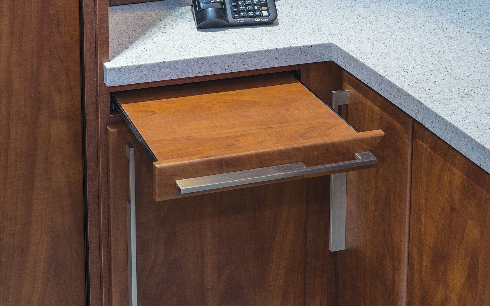 A phone sits on a counter next to a wooden drawer