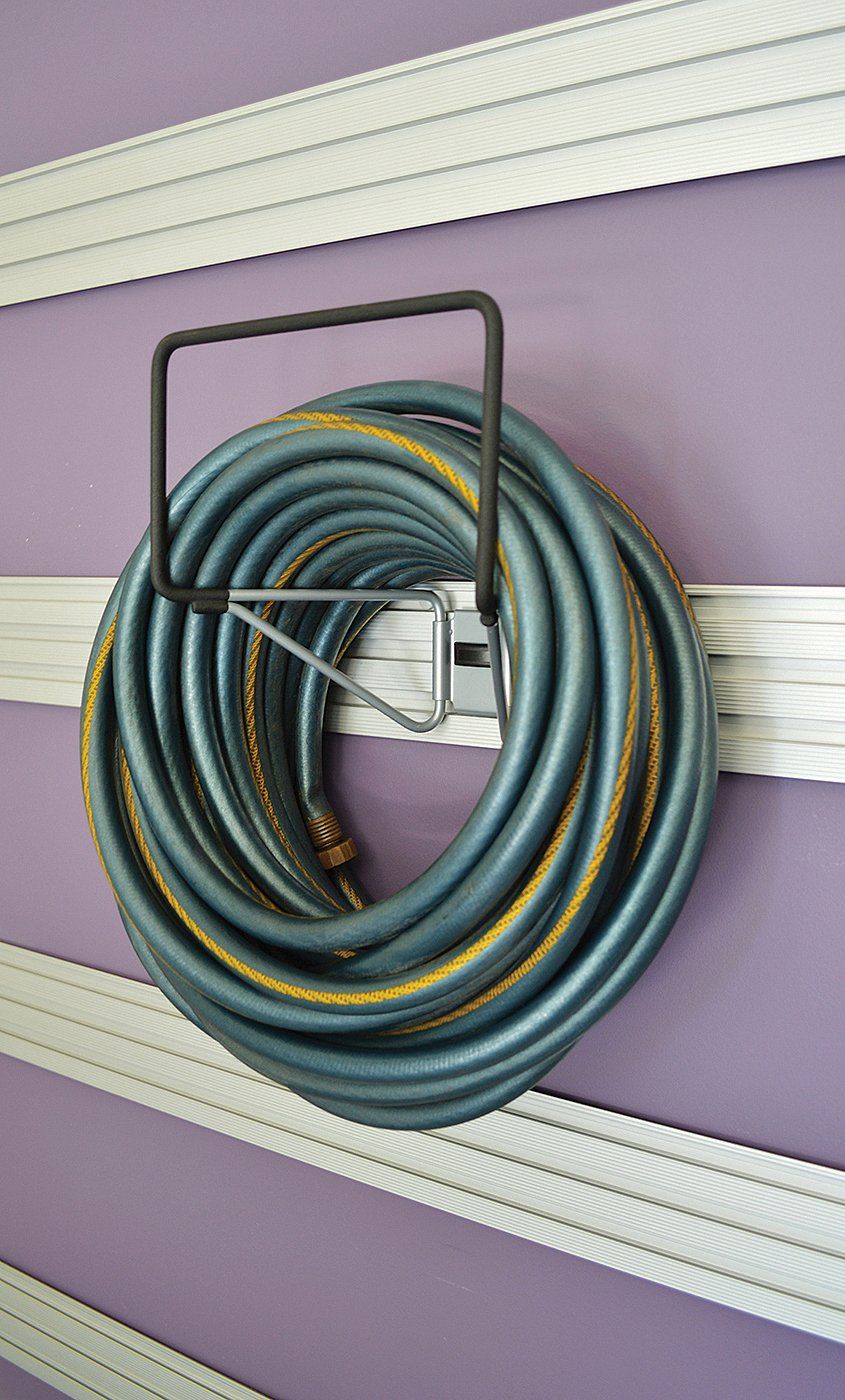A hose is hanging on a hook on a purple wall.