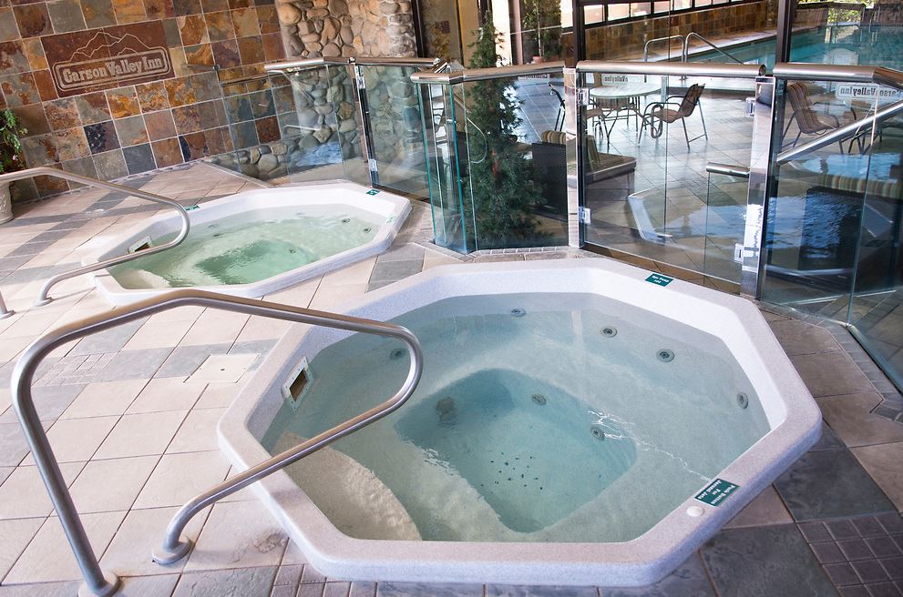 Two hot tubs in a spa setting with stone walls and glass partitions.