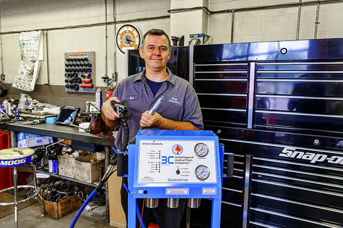 Mechanic in auto shop holding tool, standing by blue machine and tool chest.