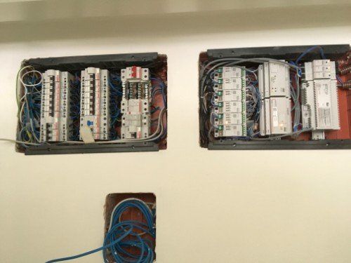Quadri elettrici aperti con fili e interruttori automatici su una parete, più una piccola bobina di cavo blu sottostante.