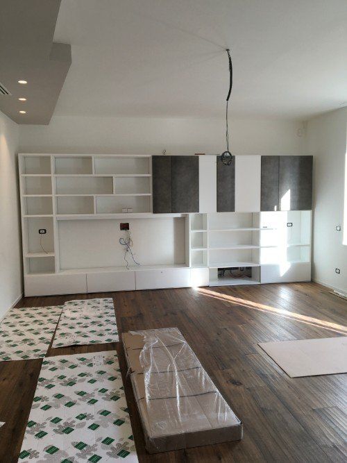 Soggiorno non rifinito con armadi a muro, pavimento in legno e materiali già predisposti per l'installazione.