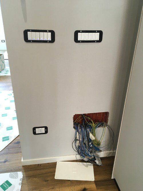 Parete interna con cavi elettrici e prese a vista sopra un pannello a pavimento in un corridoio.