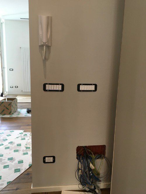 Parete con fori per interruttori elettrici e fili scoperti vicino a una porta in un interno di casa