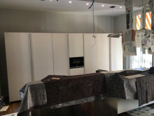 Cucina moderna in fase di ristrutturazione con mobili, ripiani coperti e cavi sospesi a soffitto.
