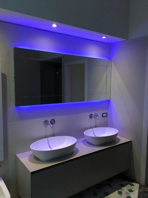 Mobile bagno moderno con due lavabi a ciotola bianchi, specchio e illuminazione a LED blu.