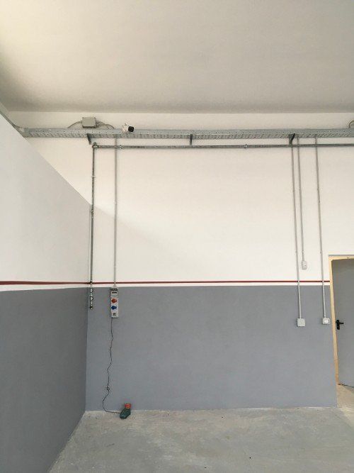 Garage vuoto con pareti grigie, tubi a soffitto e un cavo di illuminazione sospeso.