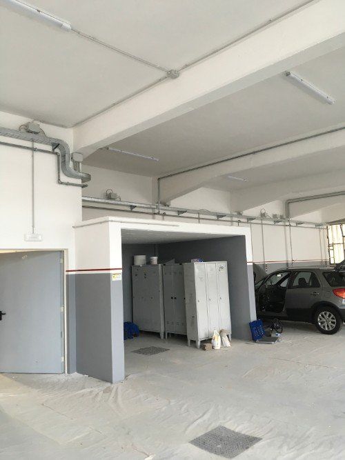 Garage interno con auto parcheggiata, armadio a muro e pareti grigie sotto un soffitto alto