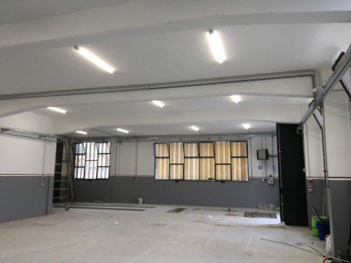 Interno di un garage vuoto con luci a soffitto bianche, pareti grigie e finestre lungo la parete di fondo.