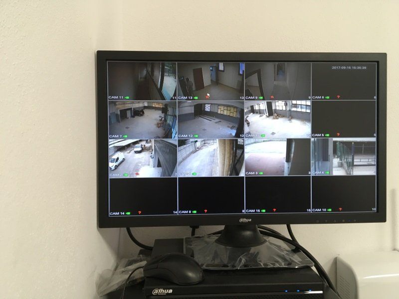 Monitor di sicurezza che mostra le immagini di diverse telecamere a circuito chiuso all'interno di una stanza, con una scrivania nera sottostante.