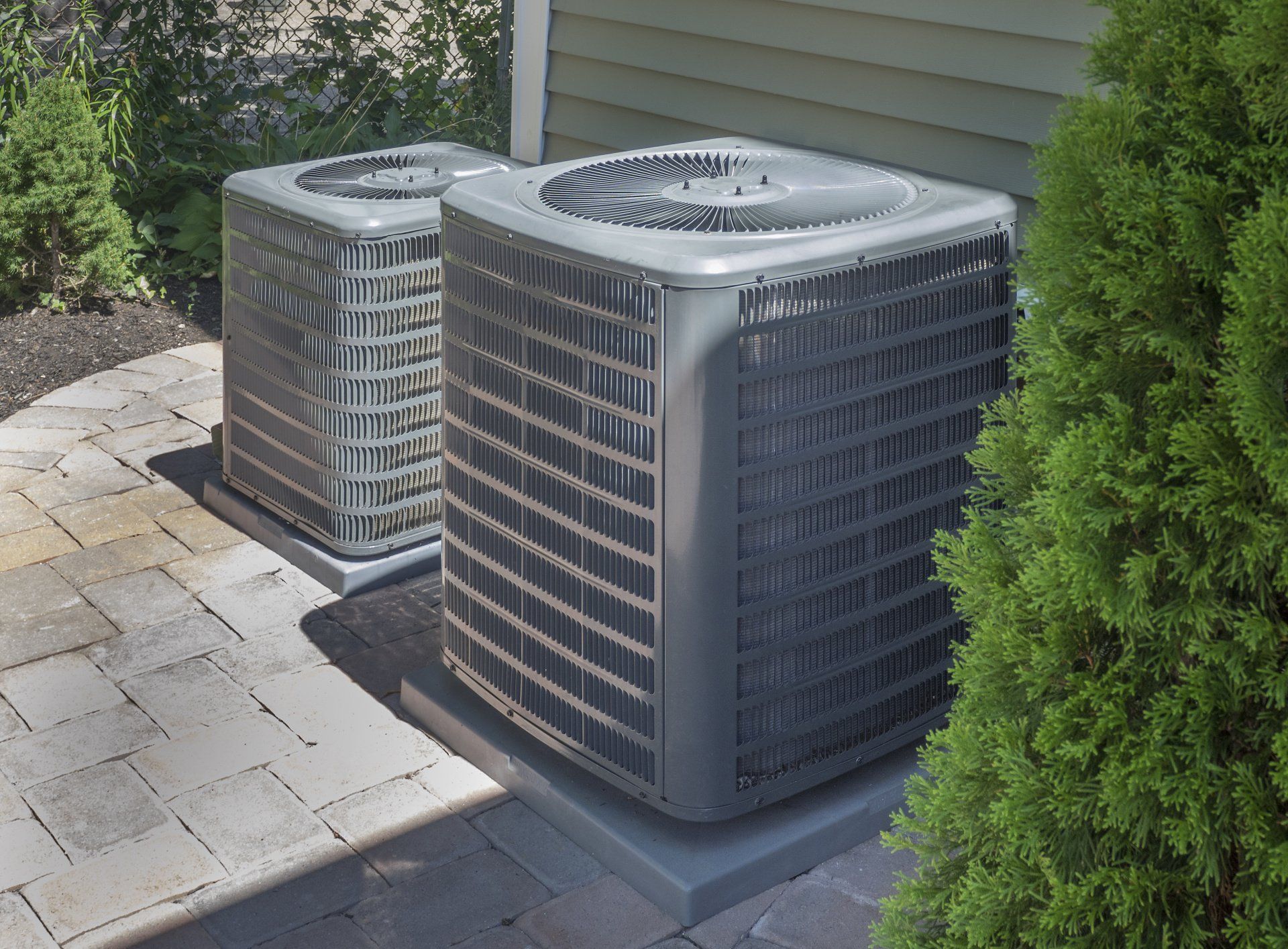 Two air conditioners are sitting on the side of a house.