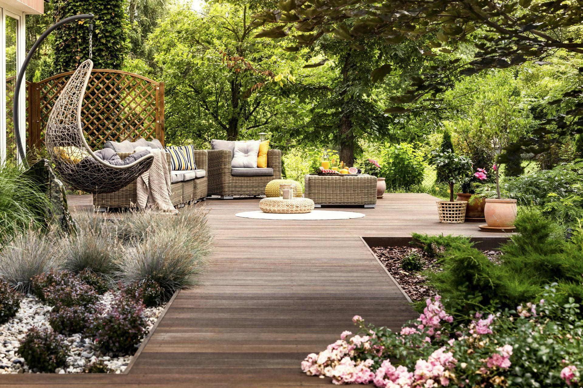 A wooden deck with a wicker chair , couch , and table in a garden.