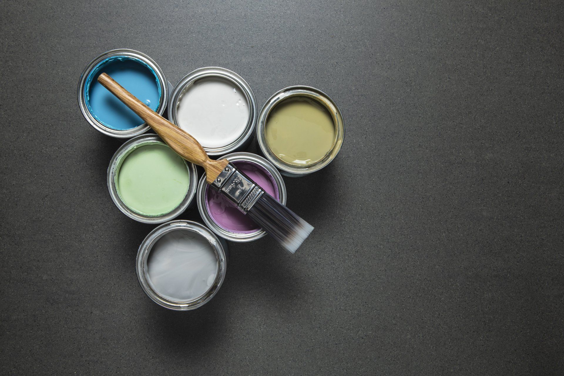 A brush is sitting on top of a bunch of paint cans.