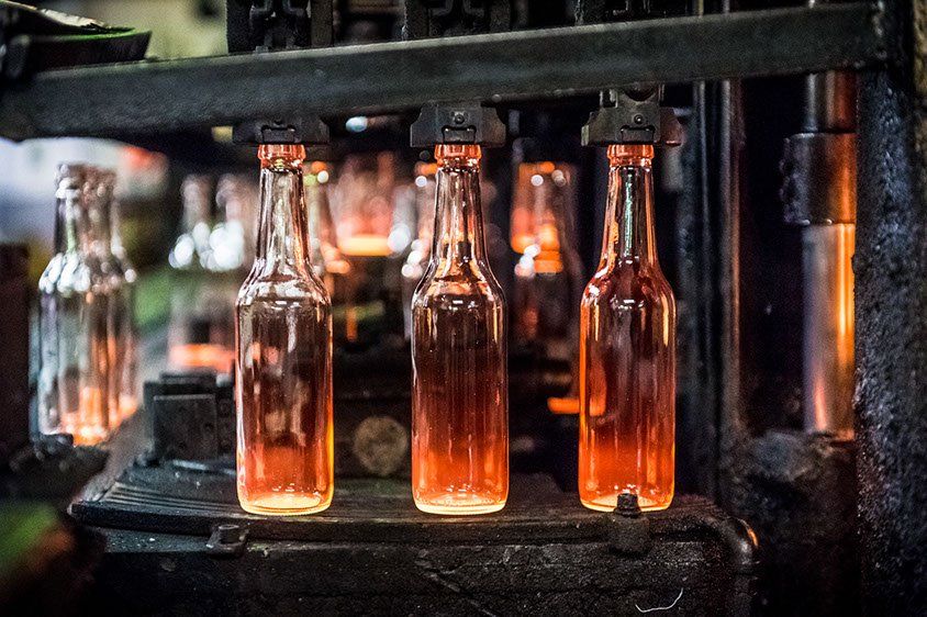 Gloeiendhete glazen flessen staan ​​op een rij op een industriële glasproductielijn O-I Maastricht.