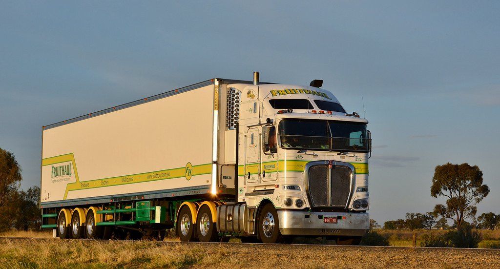 White and green semi-truck driving on a road, with a white trailer. Yellow accents.
