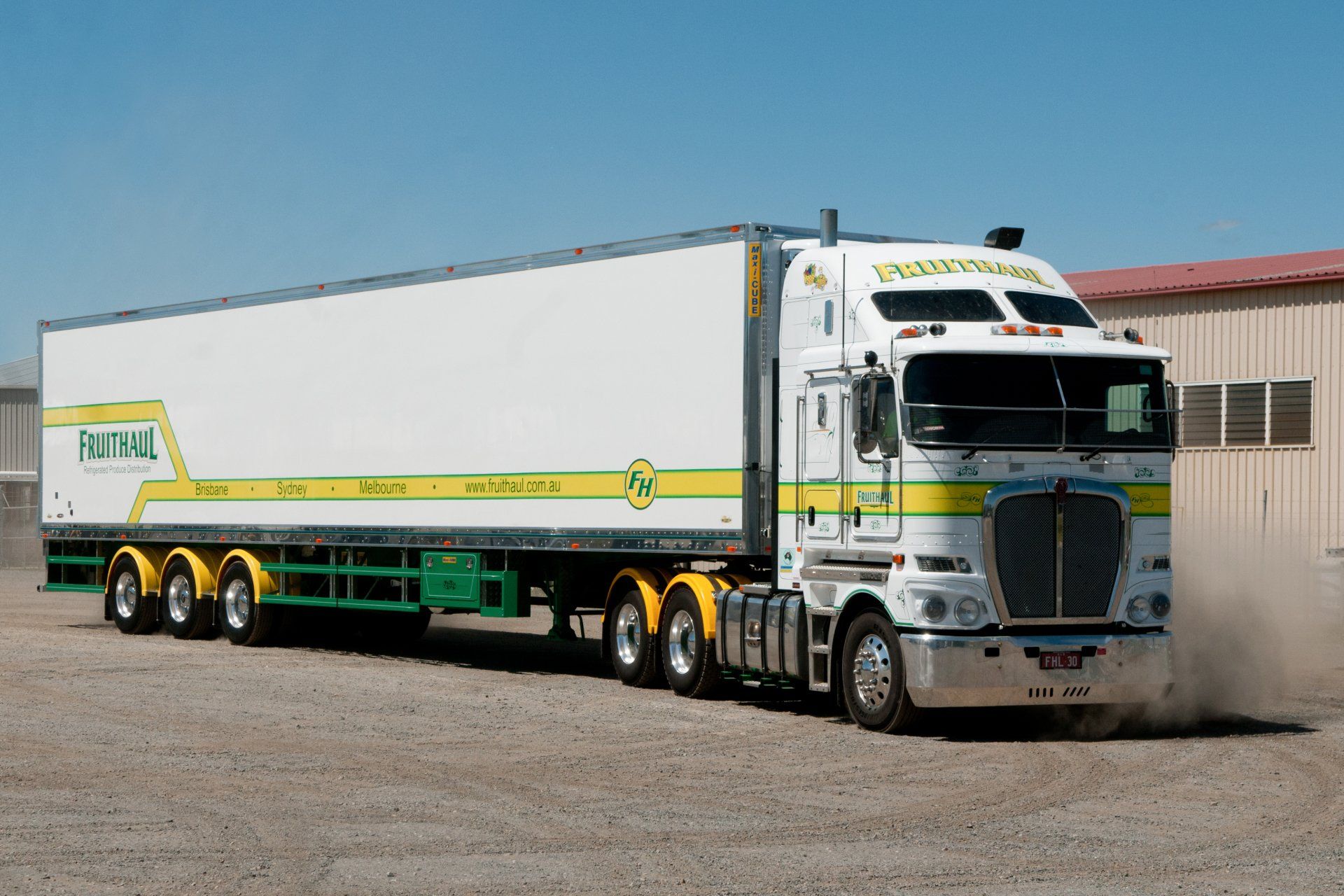 White semi-truck with green and yellow accents on a paved area, kicking up dust.