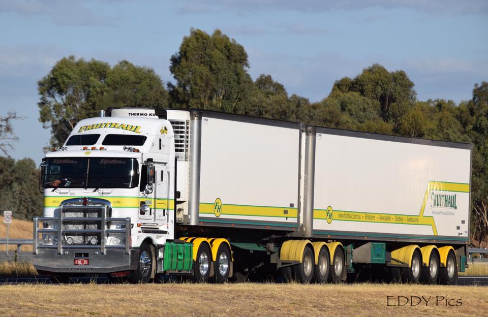 White and yellow semi-truck driving on a highway. Two white trailers with green trim.