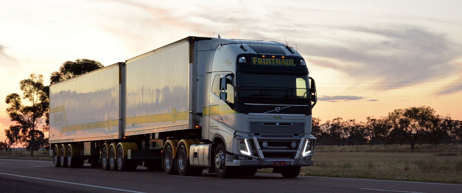 Semi-truck driving on a road at sunset.