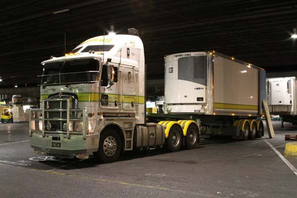 White semi-truck with a refrigerated trailer parked in a dimly lit warehouse setting.