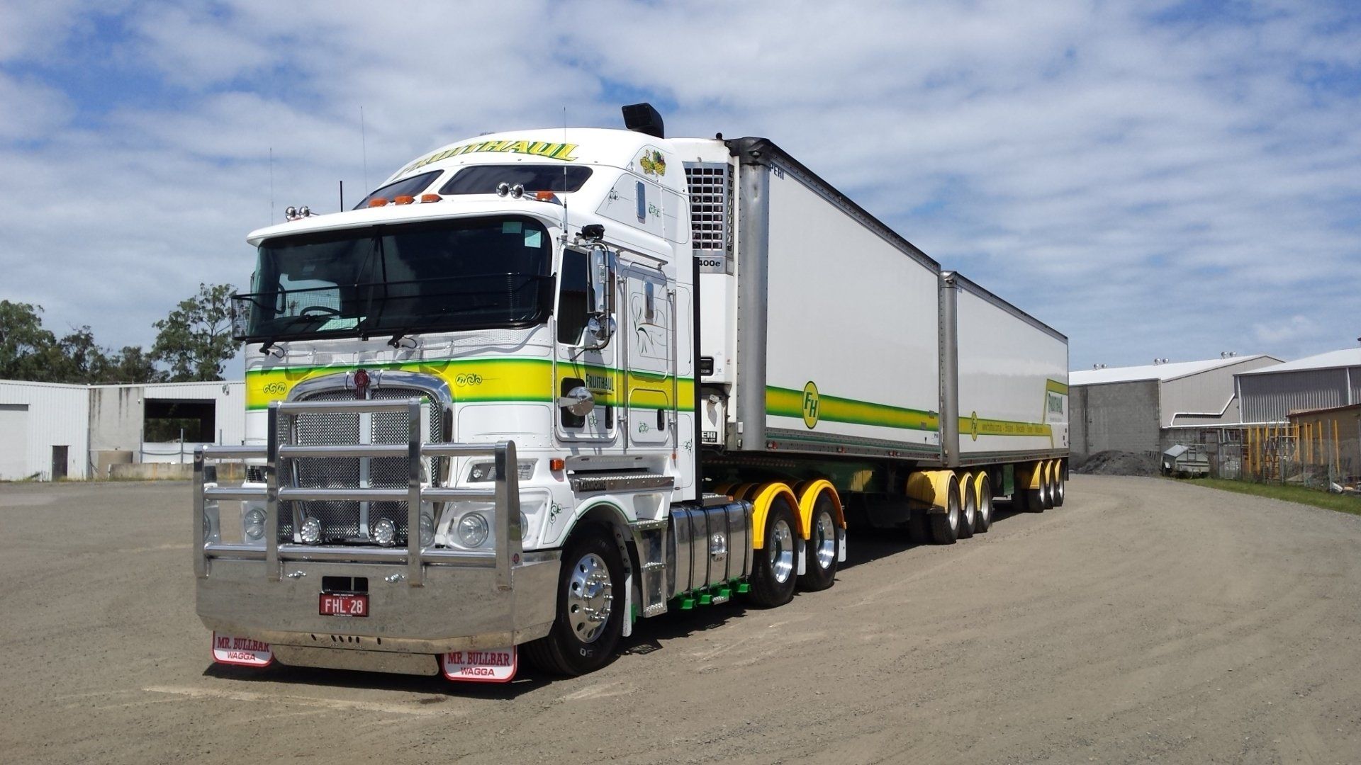 White semi-truck with two trailers, green and yellow accents, parked on a paved lot.