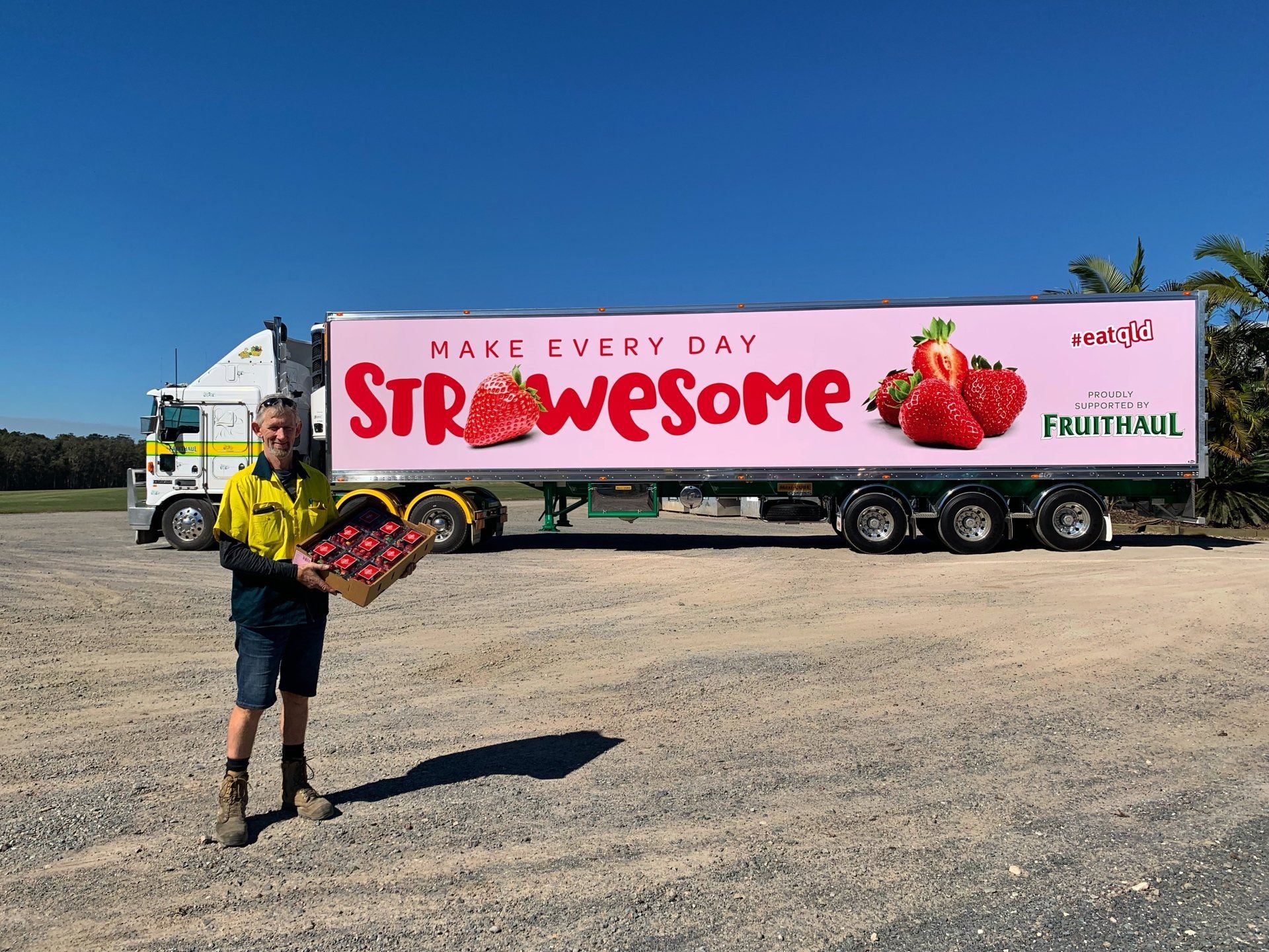 Man with a strawberry crate stands next to a truck with