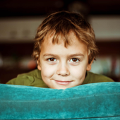 A young boy is peeking out from behind a blue blanket.