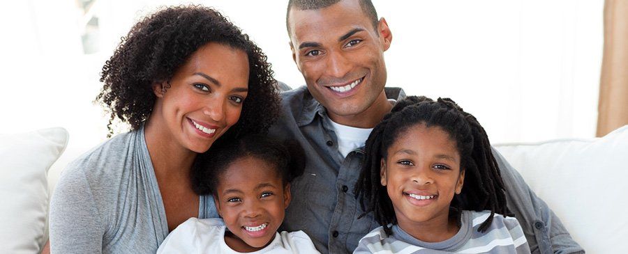 Family of four smiling on a couch, indoors. Two children, two adults.