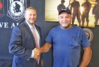 A criminal defense attorney shaking hands with a happy client in front of a sign that says we all