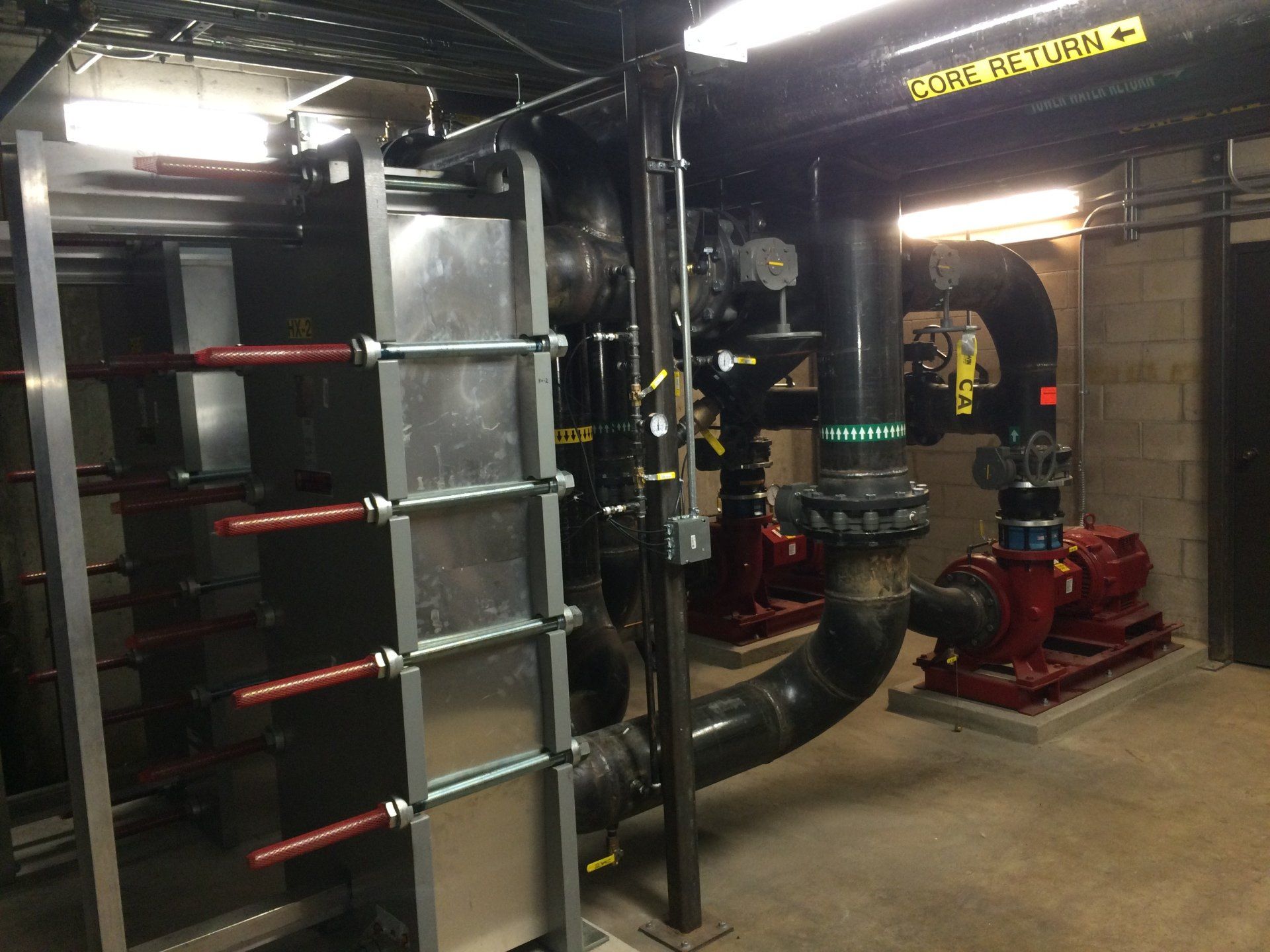 Industrial mechanical room with pipes, red pumps, and a large heat exchanger.