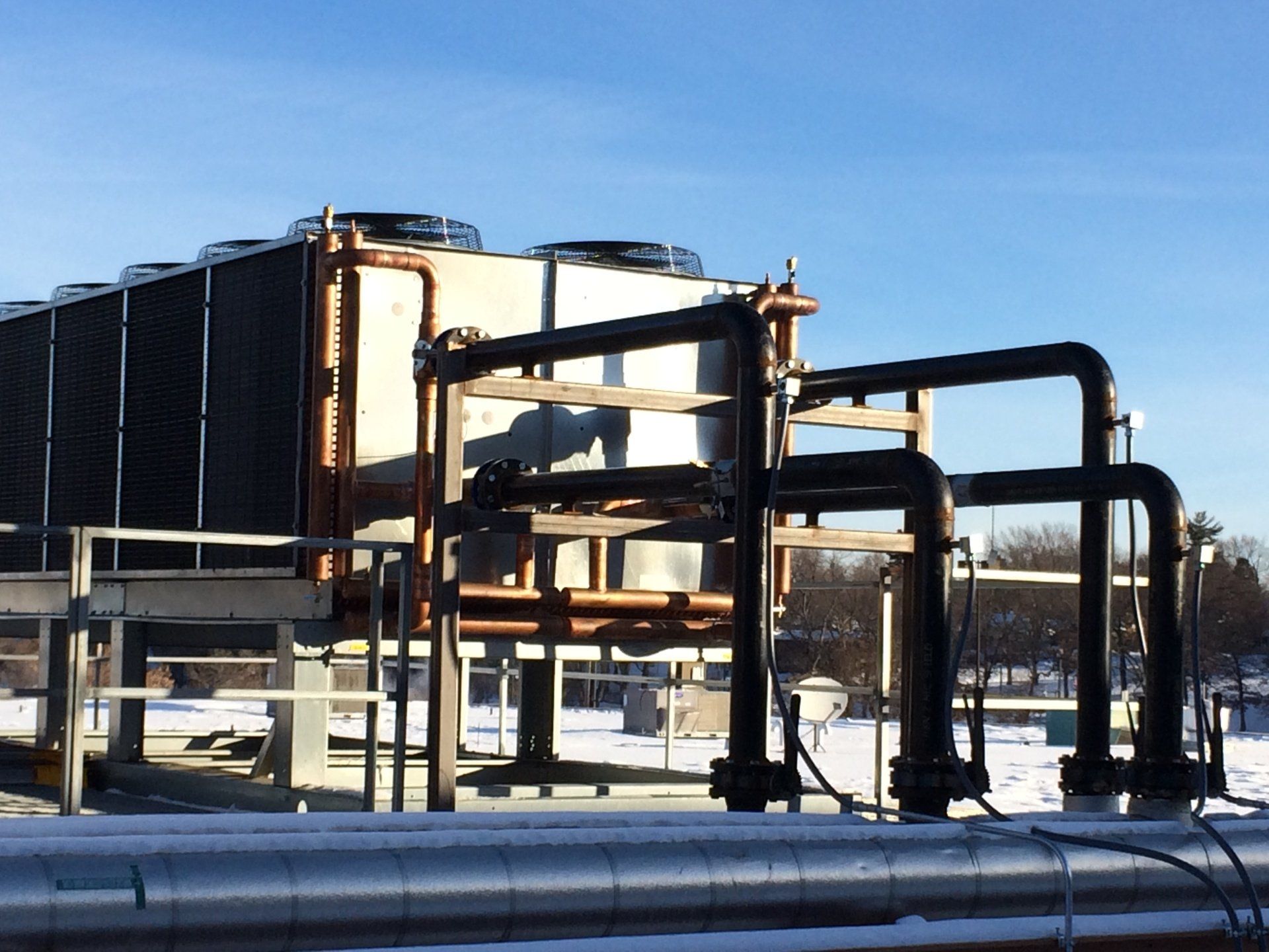 Cooling tower system outdoors on a sunny, snowy day. Metal pipes and structure; blue sky.