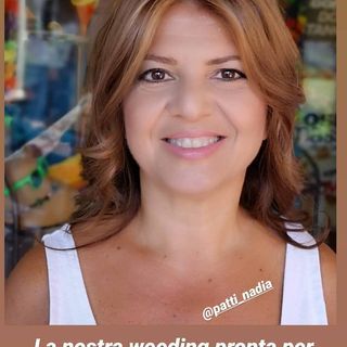 Donna con i capelli lunghi fino alle spalle e mèches, sorridente, con un top bianco. Appare 