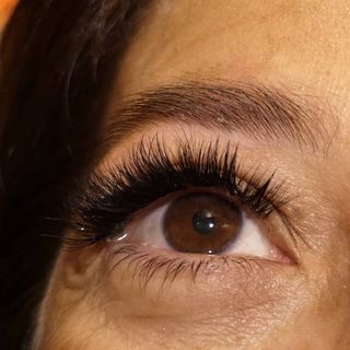 Primo piano di un occhio marrone con lunghe ciglia scure e un sopracciglio curato.
