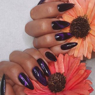 Mani con lunghe unghie a mandorla, di colore viola scuro e nero, che tengono fiori arancioni.