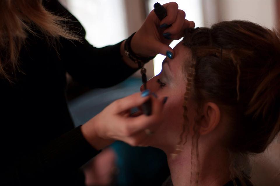 Truccatore che applica il trucco sul viso di una persona; ambientazione interna, primo piano di mani e viso.