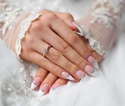 Mani di donna con unghie dalla punta bianca, anello, appoggiate su tessuto bianco con maniche in pizzo.