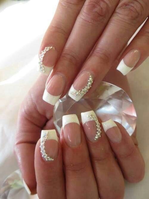 Mani con french manicure, punte bianche e impreziosite da strass, che tengono in mano un cristallo.