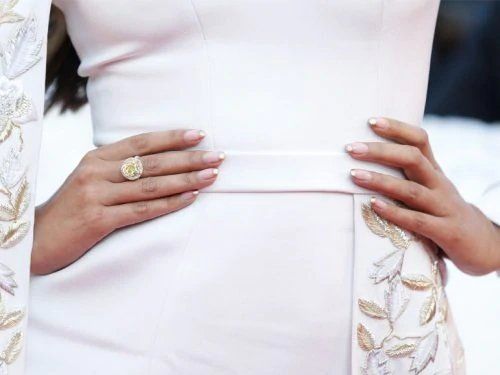 Mani di donna sulla vita di un abito bianco, che mette in mostra un grande anello di diamanti gialli e unghie con french manicure.